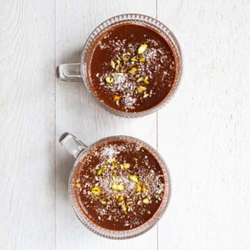 Healthy chocolate pudding topped with pistachios and coconut flakes in two glasses.