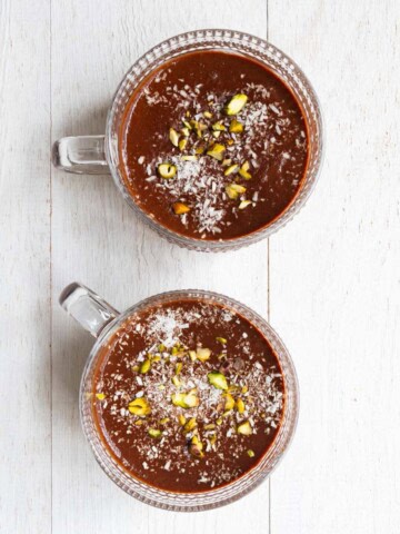 Healthy chocolate pudding topped with pistachios and coconut flakes in two glasses.