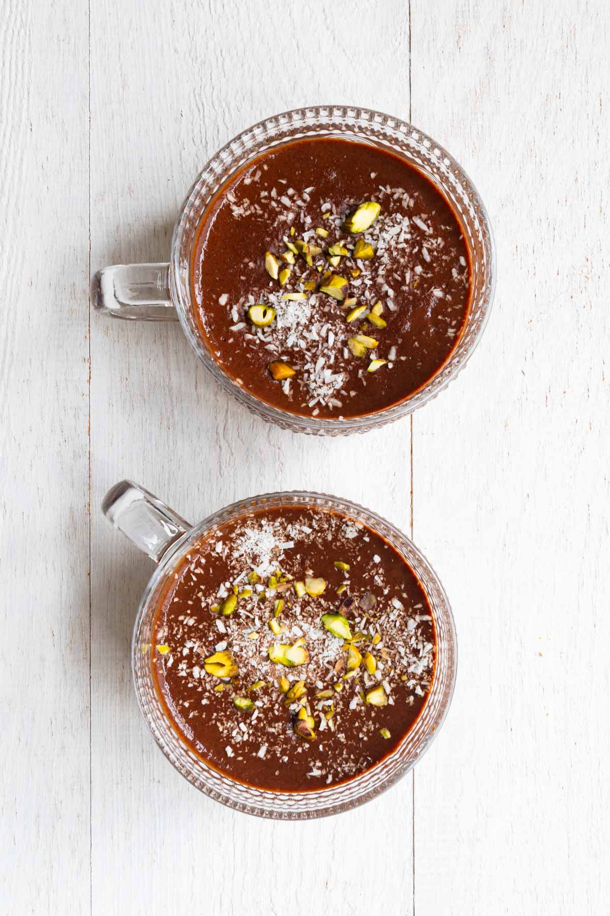 Healthy chocolate pudding topped with pistachios and coconut flakes in two glasses.