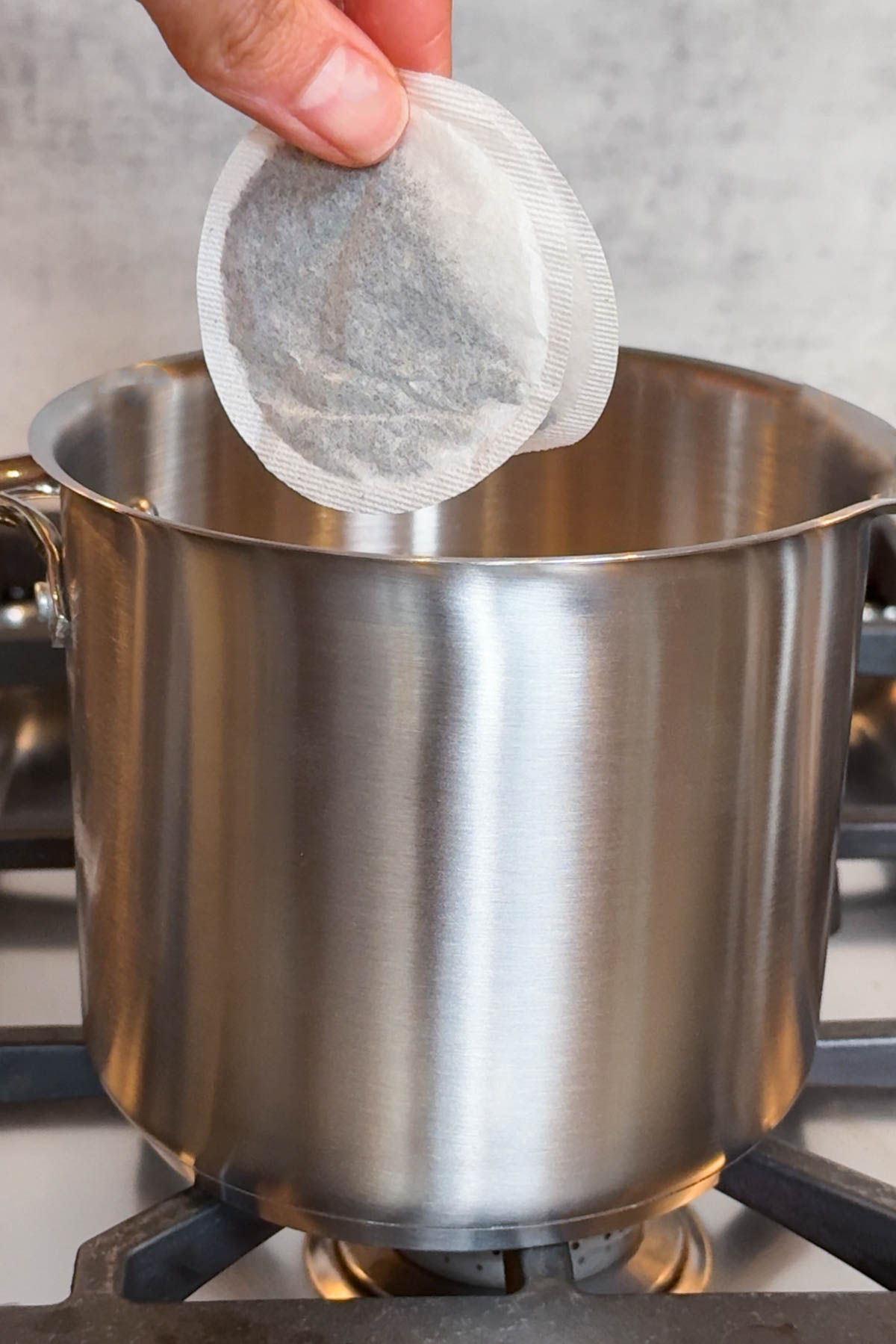 Tea bags held over a steel saucepan with a pouring spout.