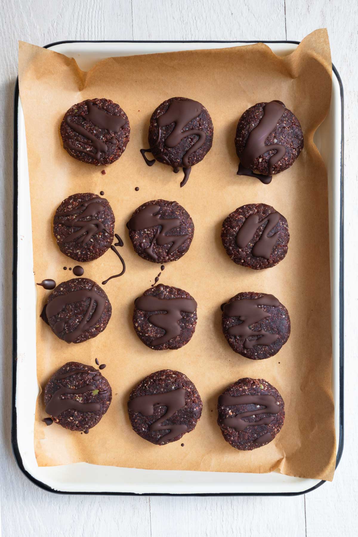 Twelve no-bake protein cookies on parchment paper drizzled with chocolate.
