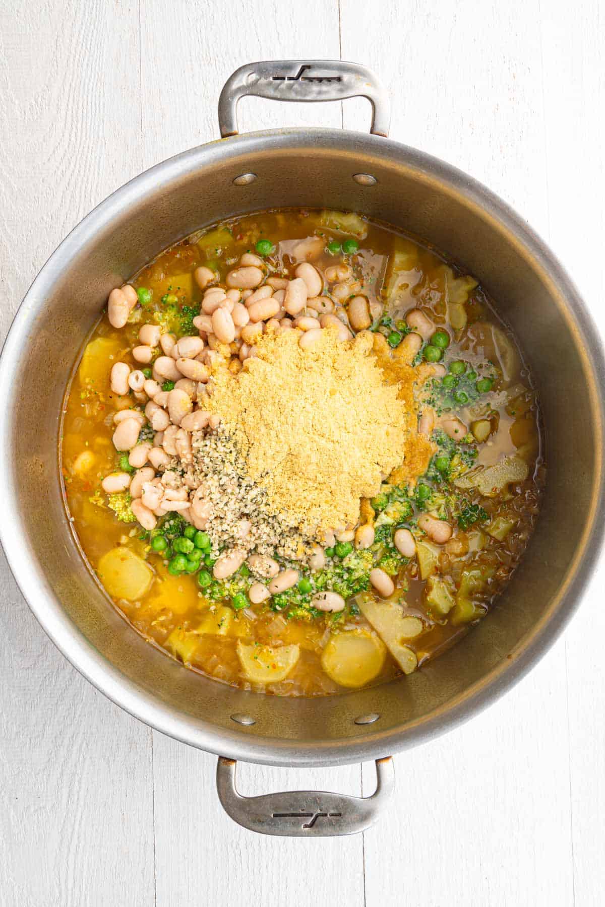 Vegetable broth, sliced broccoli stems, broccoli florets, white beans, green peas, hemp hearts, nutritional yeast, and seasoning in a large saucepan.