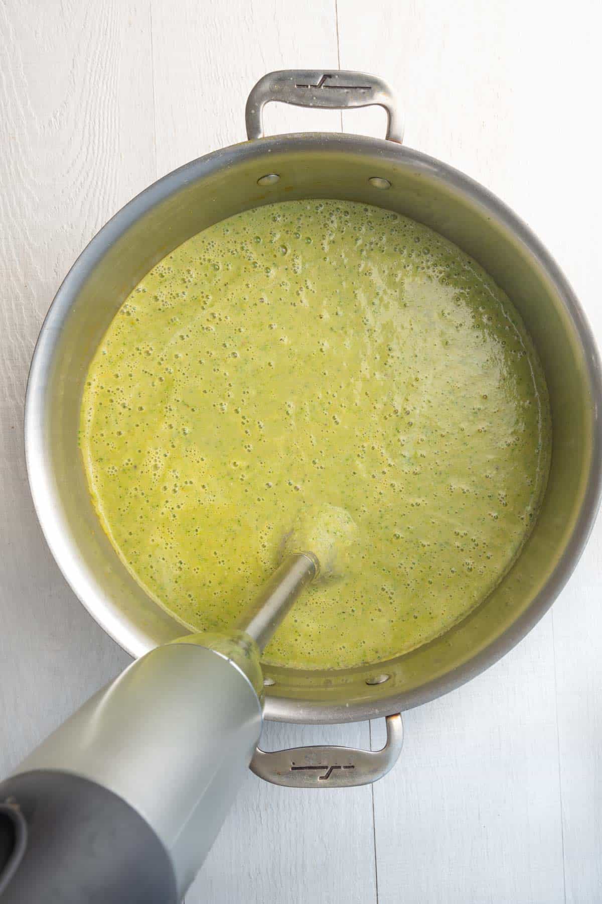 Immersion blender in broccoli soup in a large saucepan.