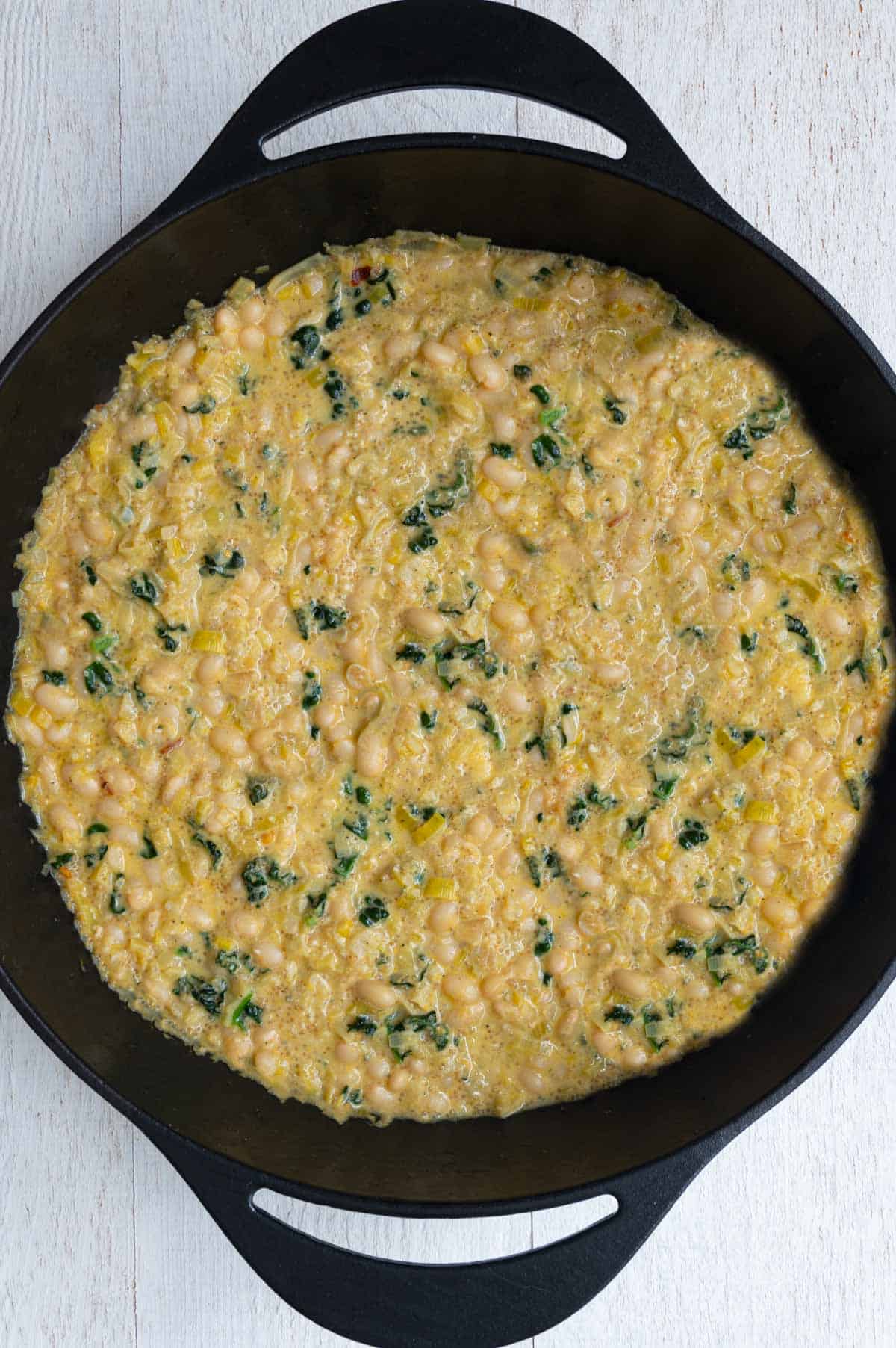 Creamy white beans with amaranth in a cast-iron skillet.