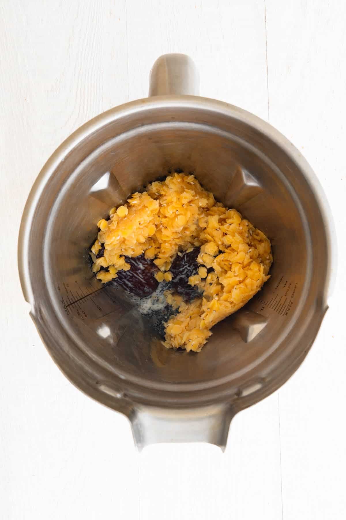 Cooked red lentils, dates, milk, and ground black sesame seeds in the canister of a blender.