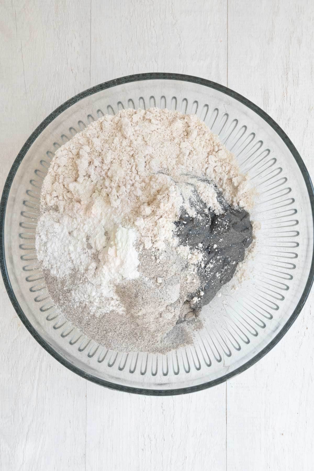 Buckwheat flour, oat flour, baking powder, baking soda, and blended black sesame seeds, lentils, and dates in a large glass bowl.