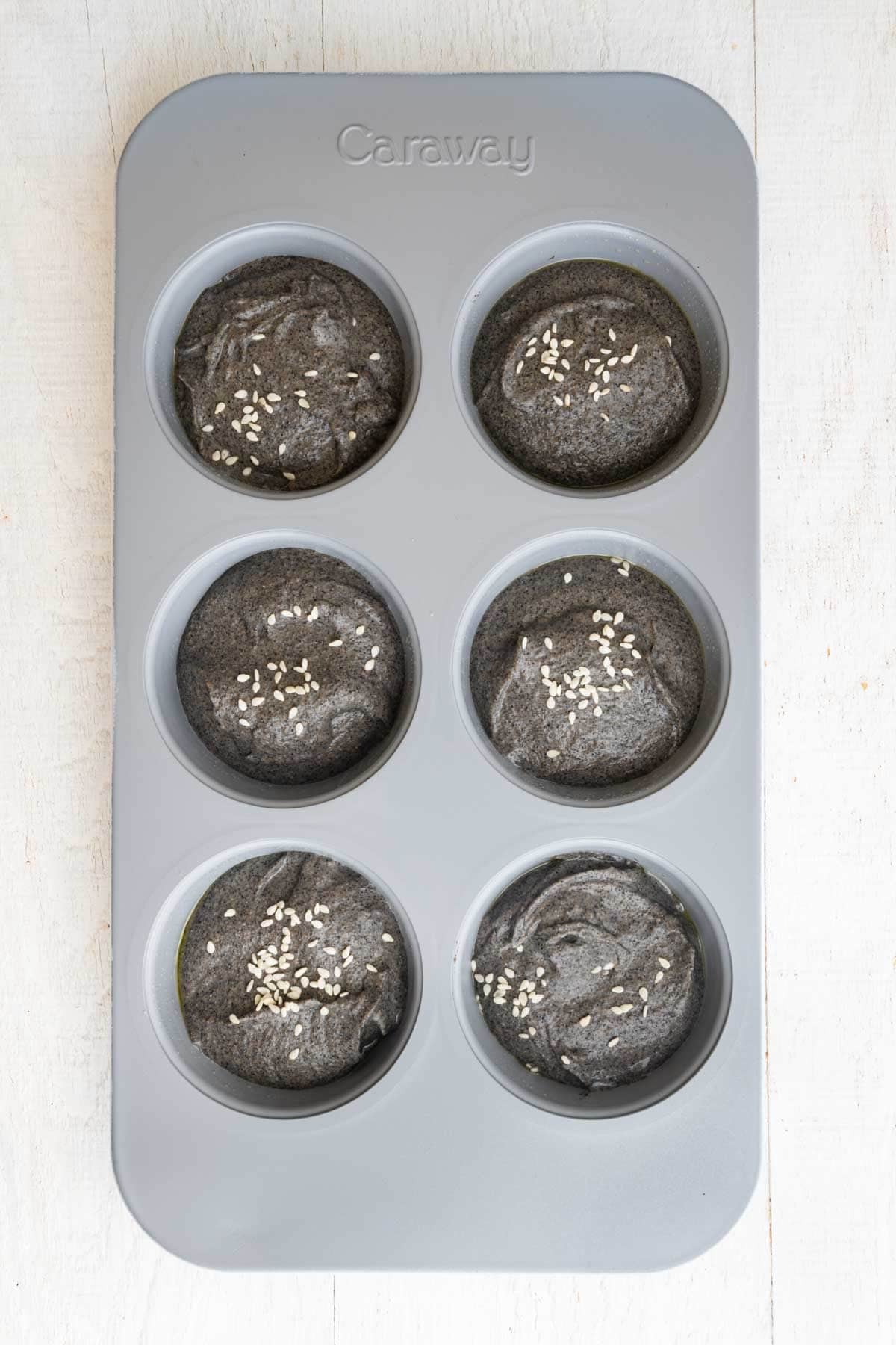 Black creamy batter in six muffin tin holder.