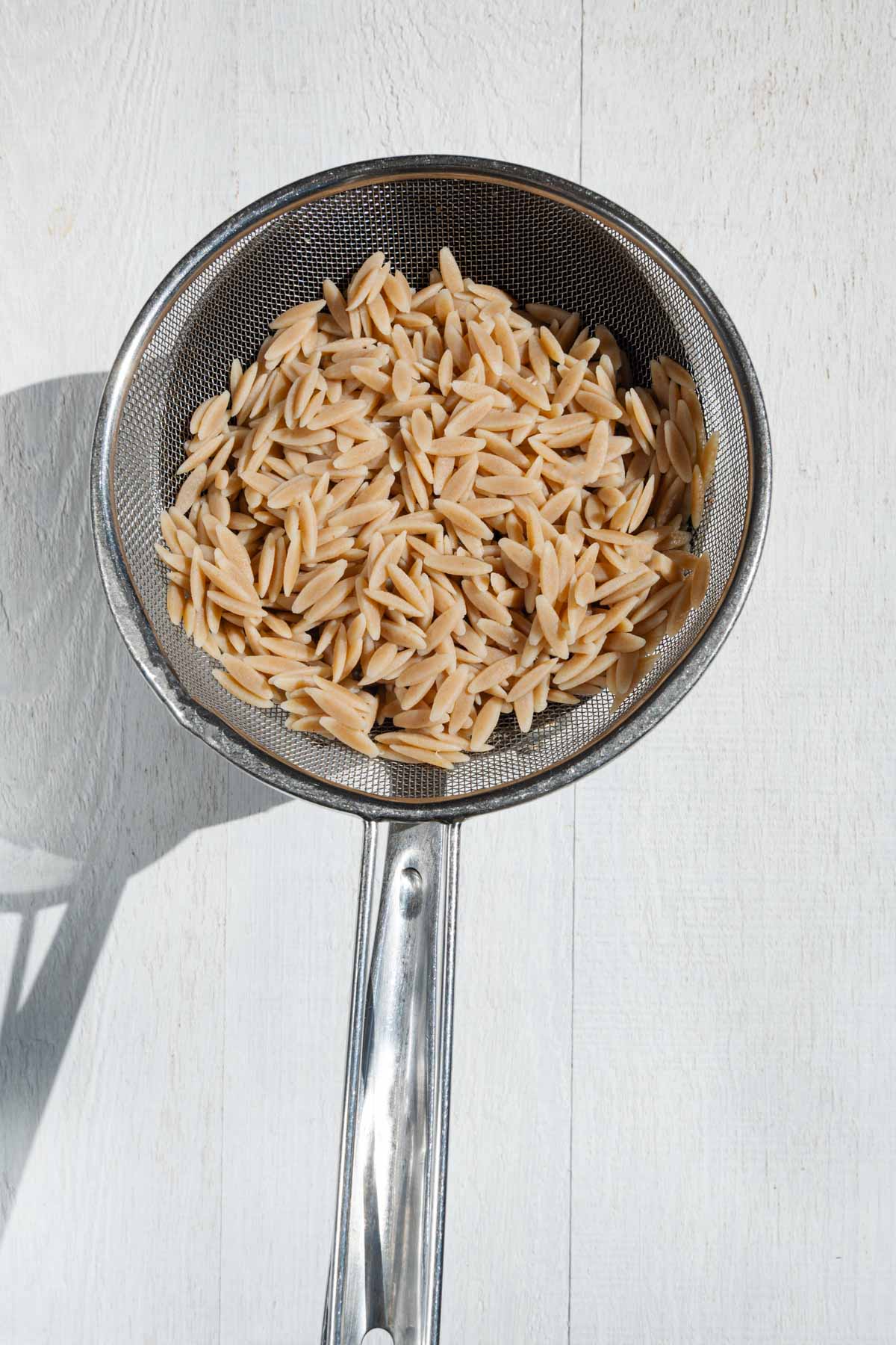 Cooked orzo in a sieve.