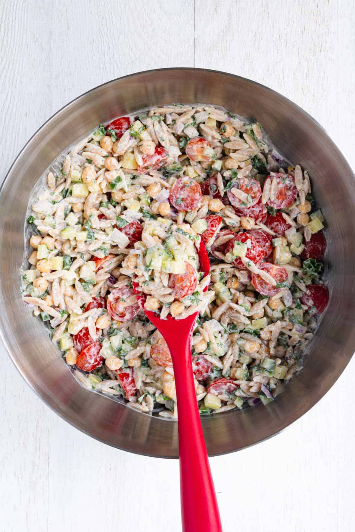 Greek Orzo Pasta Salad in a mixing bowl with a red spoon.