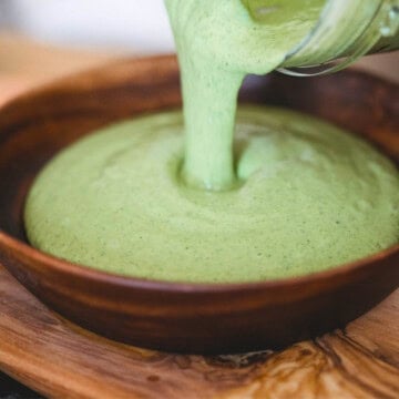 Pouring green cashew sauce into a wooden bowl.