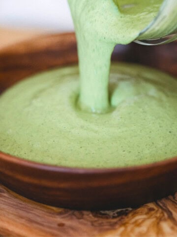 Pouring green cashew sauce into a wooden bowl.