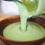 Pouring green cashew sauce into a wooden bowl.