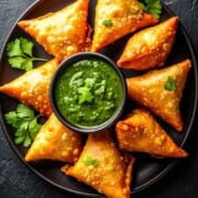 Green chutney in a bowl with crispy samosas.