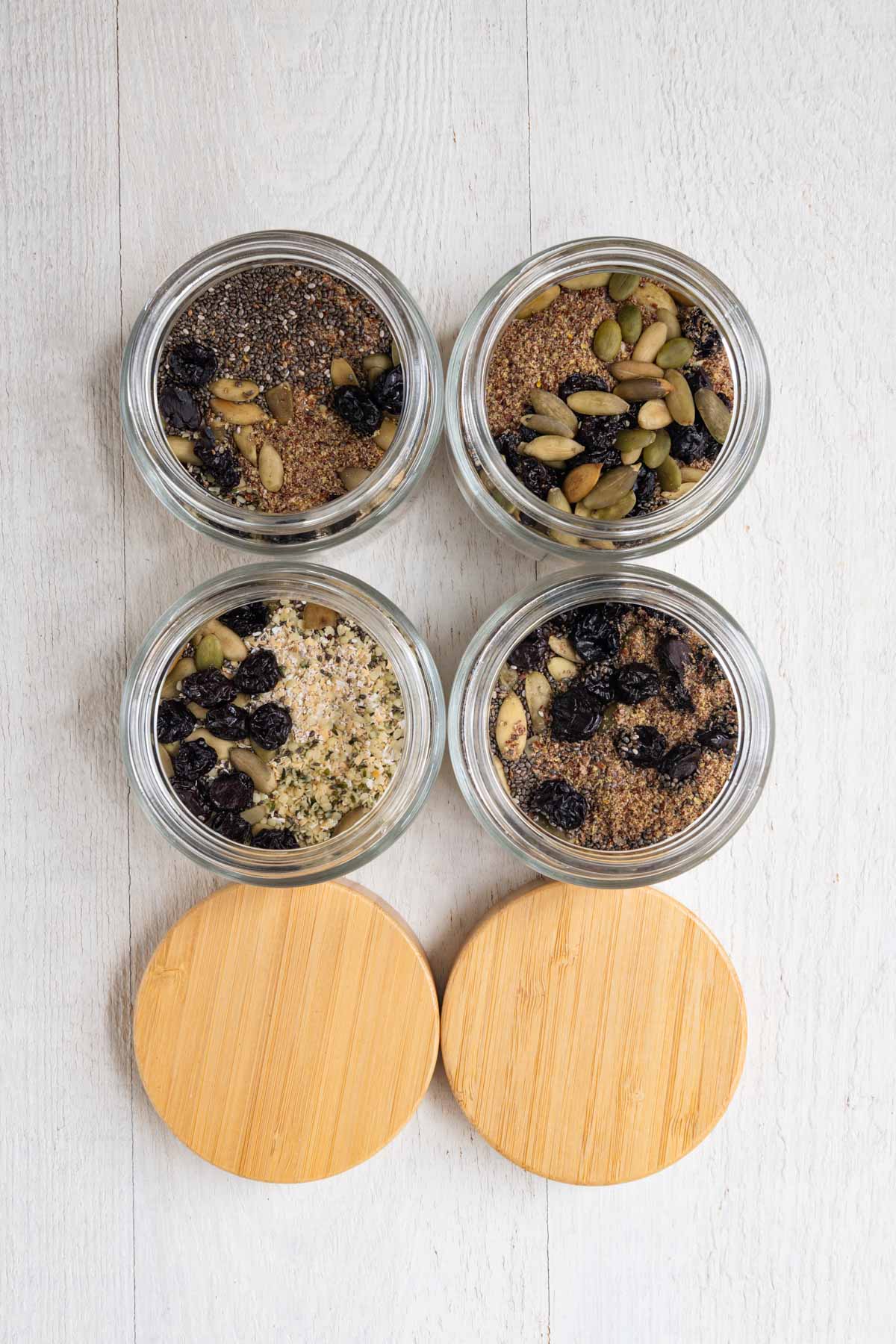 Healthy homemade muesli with ground flaxseeds, hemp hearts, dried tart cherries, prunes, oat bran, rolled oats, chia seeds, and hemp hearts in four glass jars.