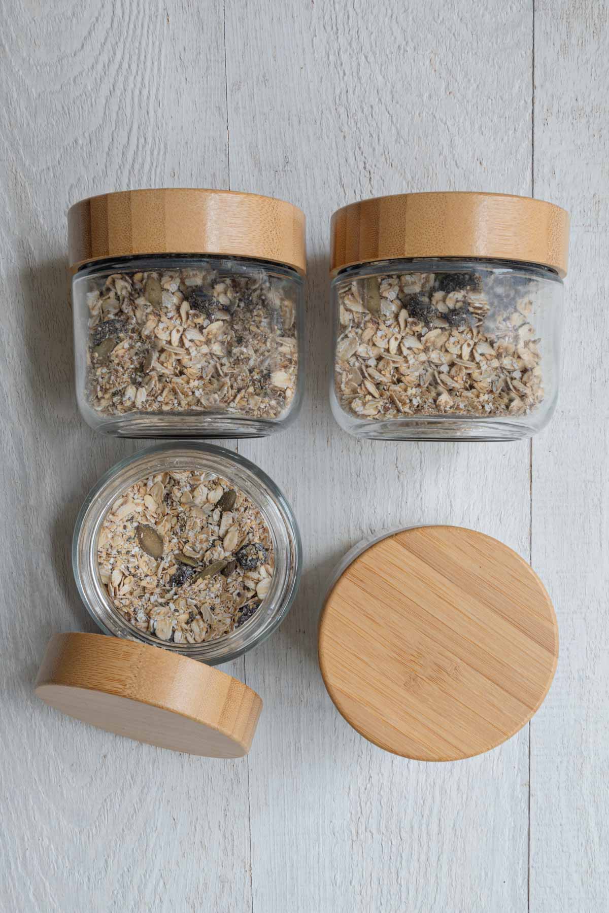 Ground flaxseeds, hemp hearts, dried tart cherries, prunes, oat bran, rolled oats, chia seeds, and hemp hearts in four glass jars.