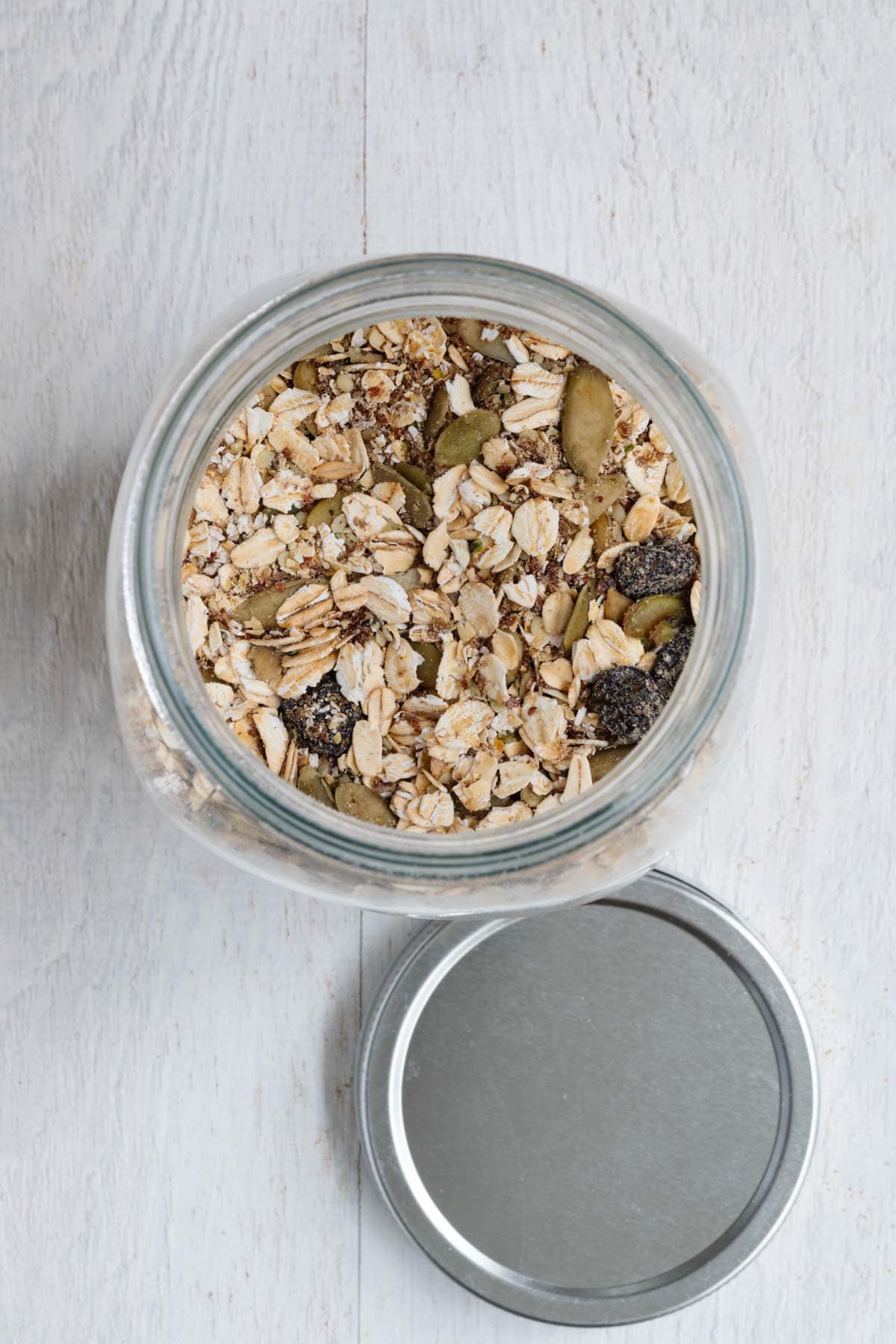Healthy homemade muesli with ground flaxseeds, hemp hearts, dried tart cherries, prunes, oat bran, rolled oats, chia seeds, and hemp hearts in a glass jar.