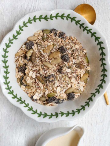 Healthy homemade muesli with ground flaxseeds, hemp hearts, dried tart cherries, prunes, oat bran, rolled oats, chia seeds, and hemp hearts in a bowl with nondairy milk.
