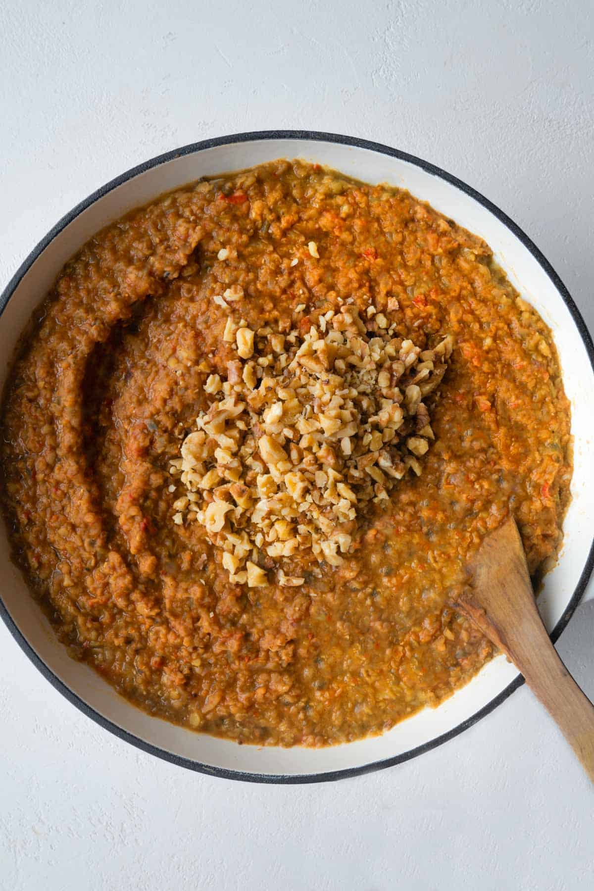 Eggplant, red lentils, broth, onion, garlic, and tomato paste cooking in a large skillet topped with chopped walnuts.
