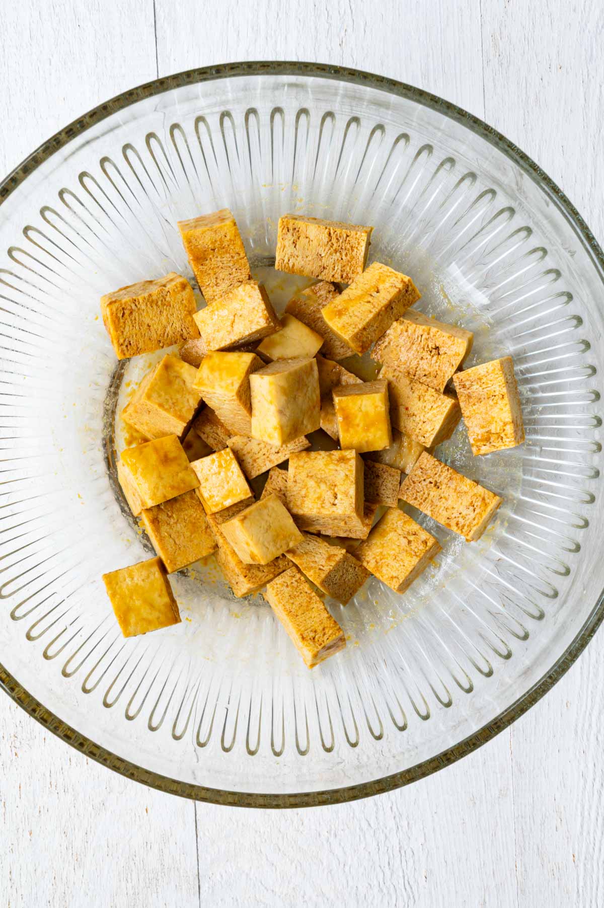 Previously frozen tofu cubes seasoned in a glass bowl.