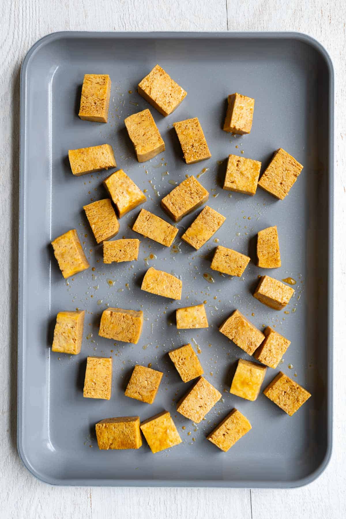 Previously frozen tofu, seasoned, on a baking sheet.