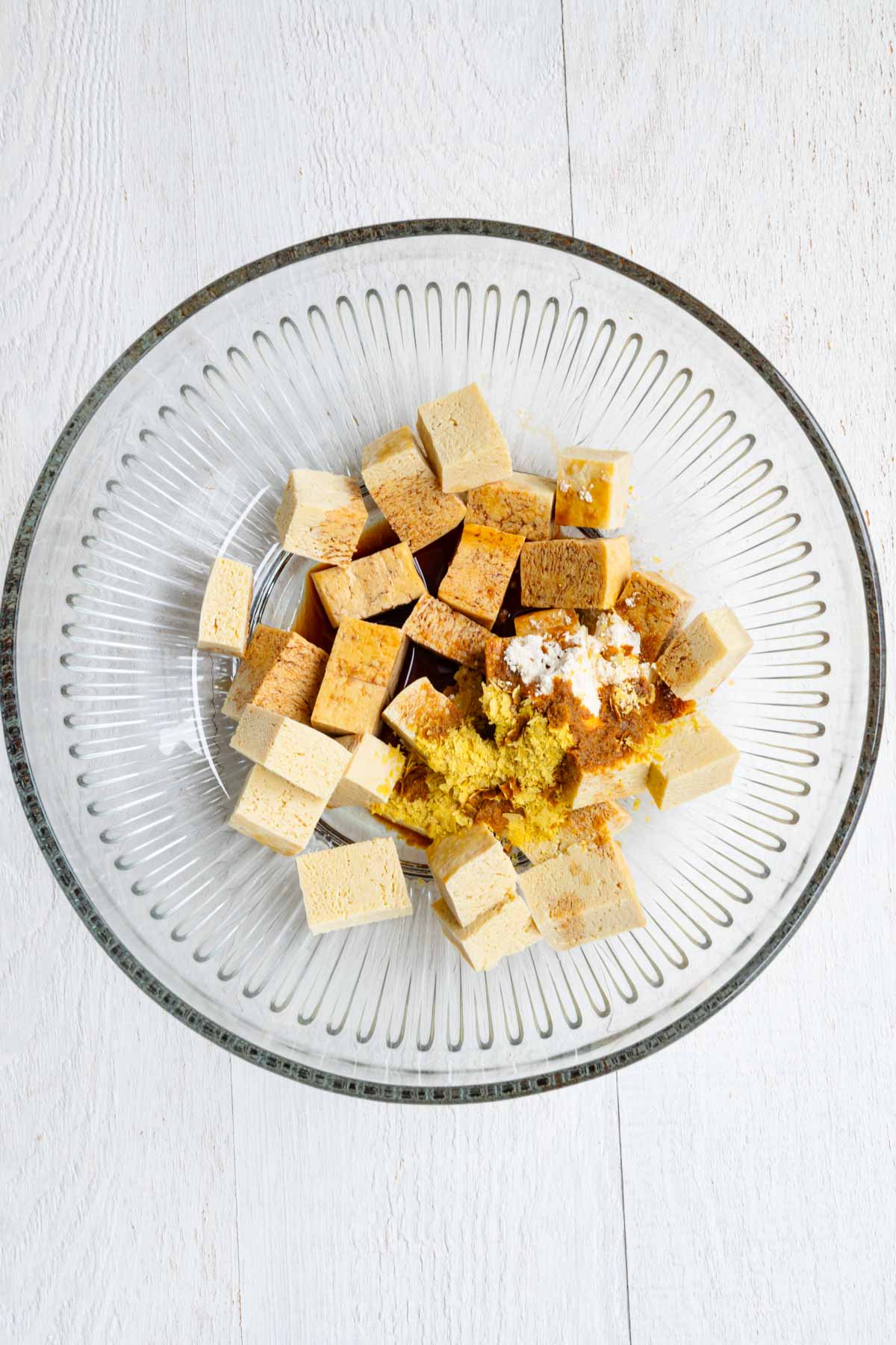 Previously frozen tofu cubes with seasoning in a glass bowl.
