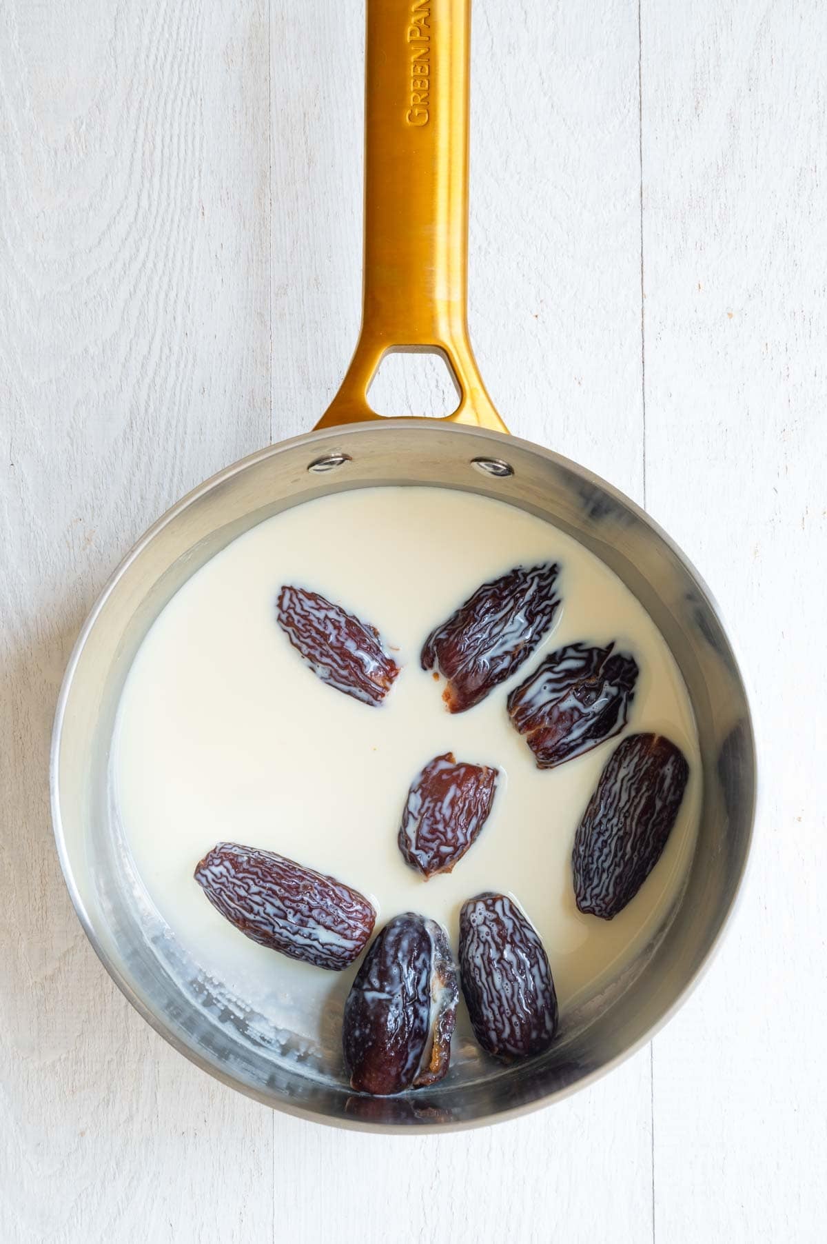 Dates soaking in warm milk in a saucepan.