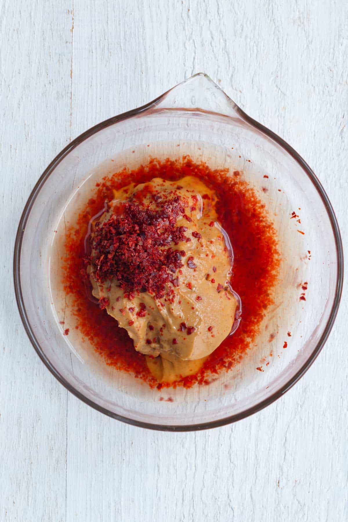 Peanut butter, Gochugaru, tamari, rice vinegar, maple syrup, and water in a glass bowl.