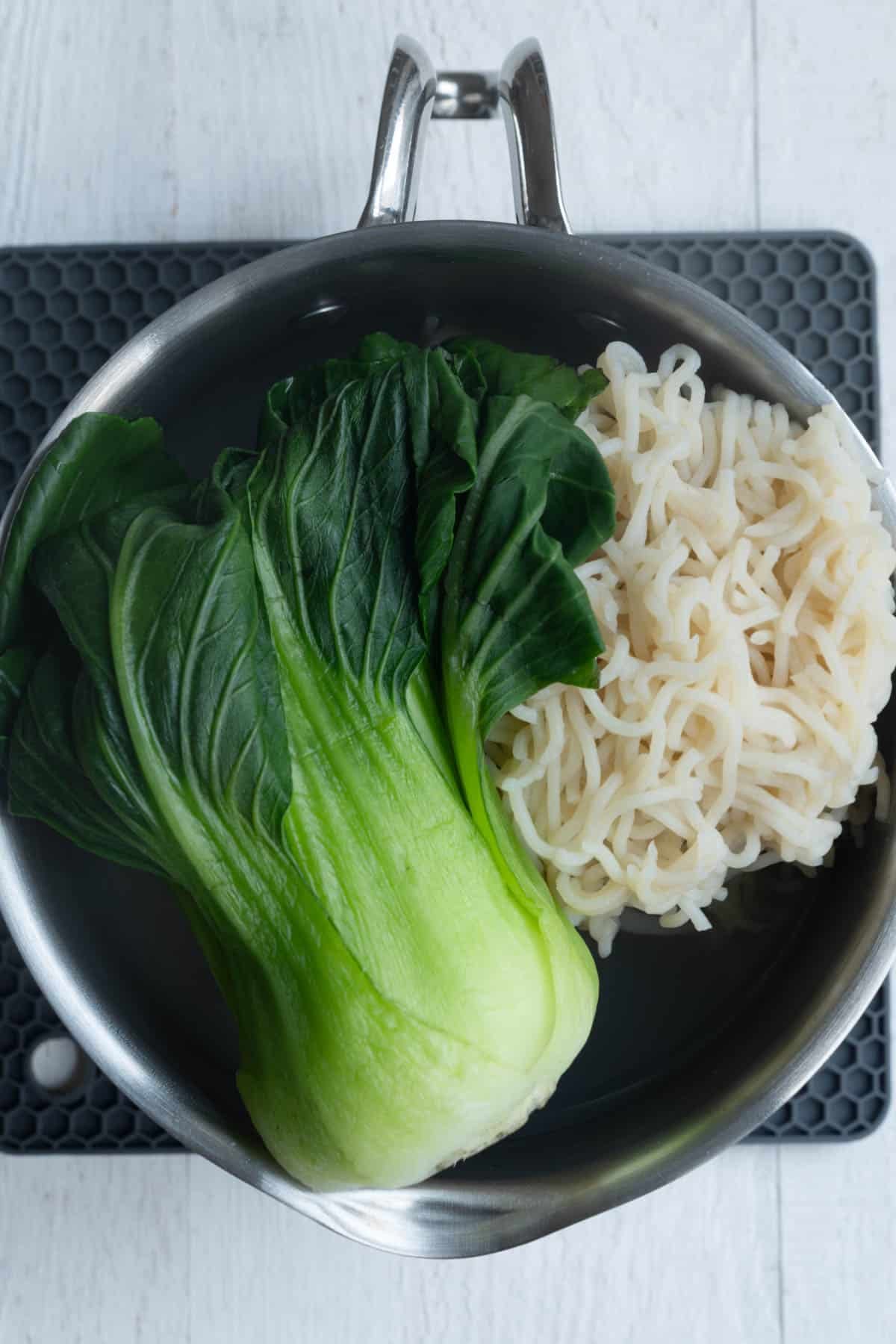 Cooked noodles and bok choy in a draining pot.