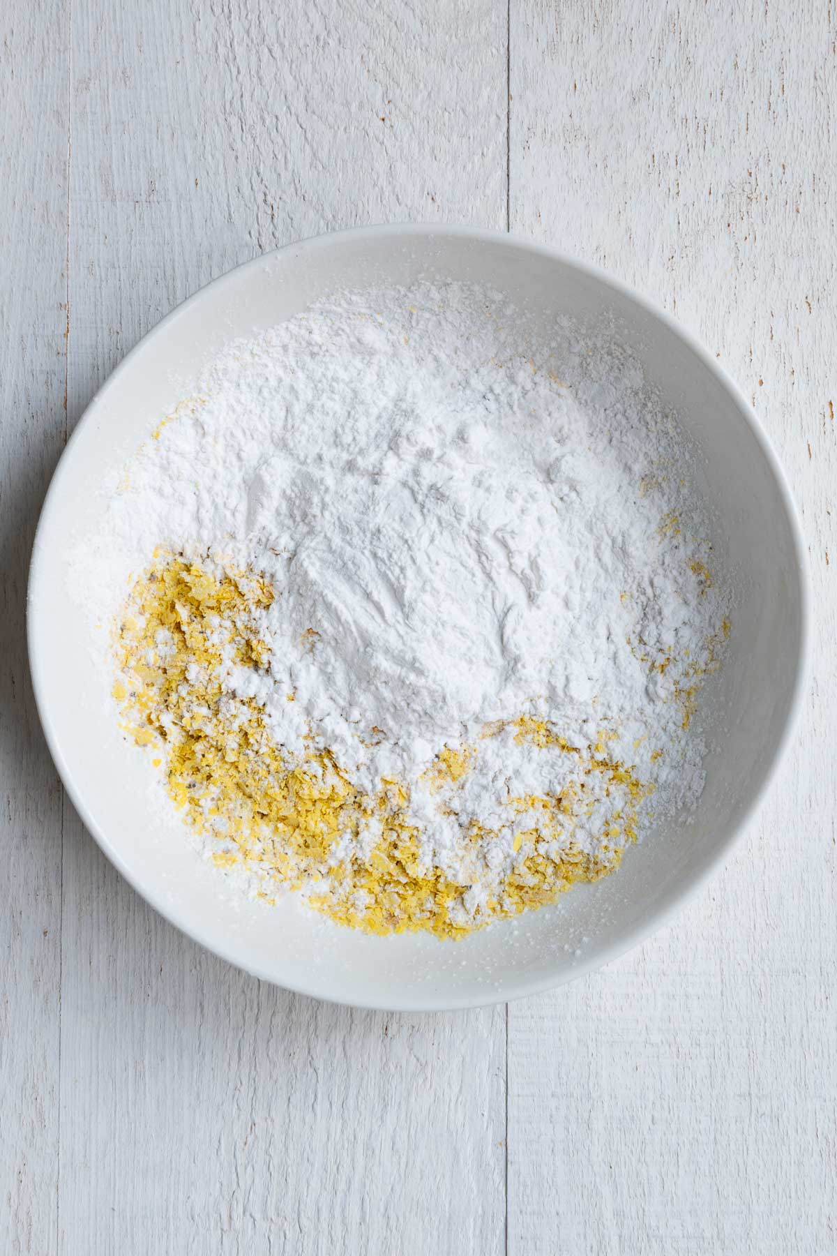 Nutritional yeast, arrowroot, tofu, garlic powder, onion powder, black pepper, and salt in a white bowl.