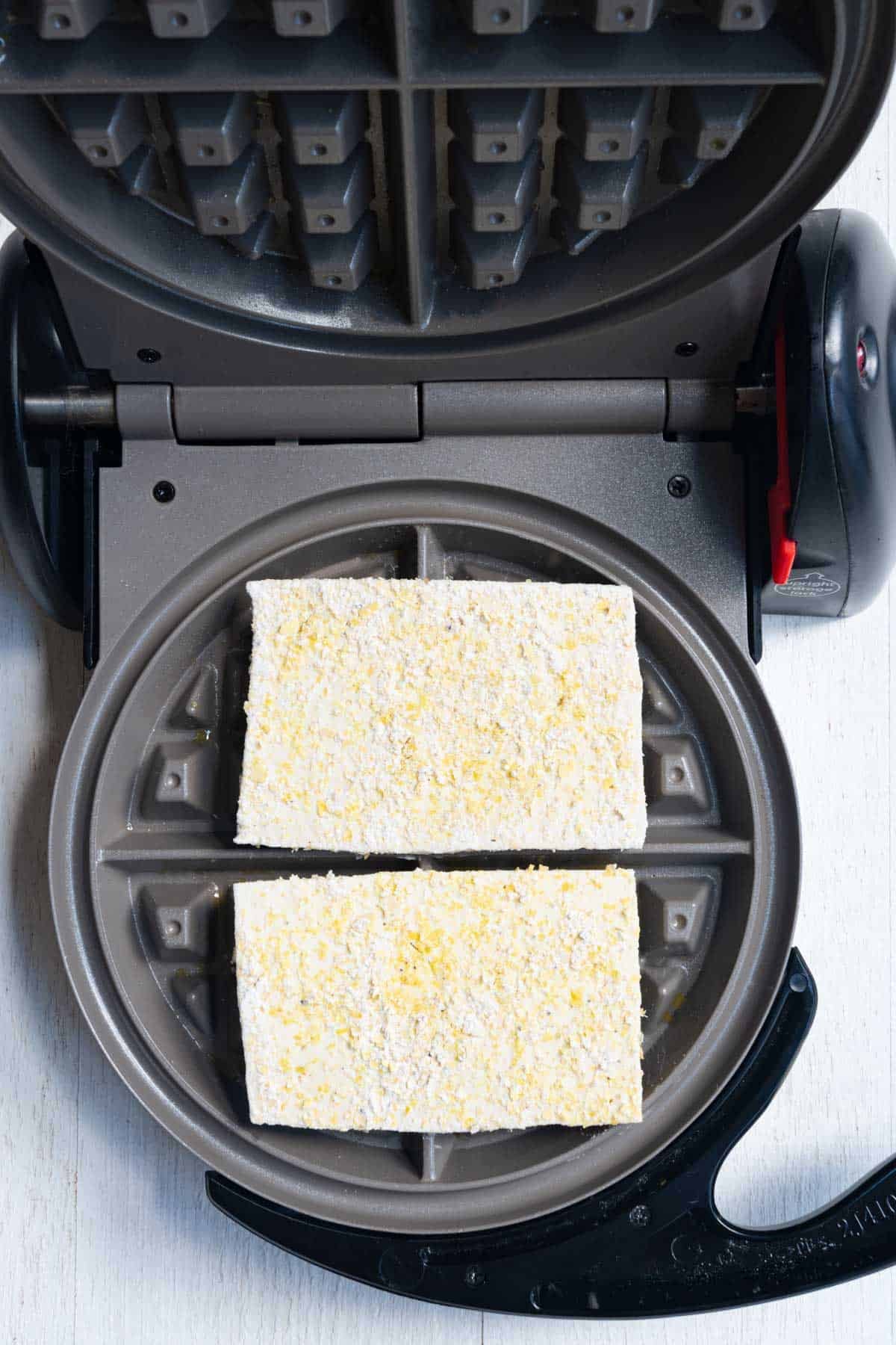 Sliced tofu coated in cornstarch, nutritional yeast, garlic and onion powder, salt, and black pepper in a waffle maker.