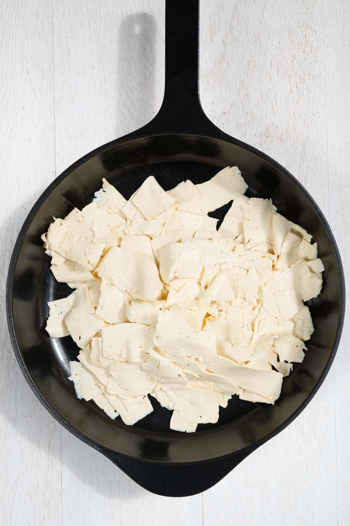 Tofu thinly sliced with a cabbage peeler in a black skillet.
