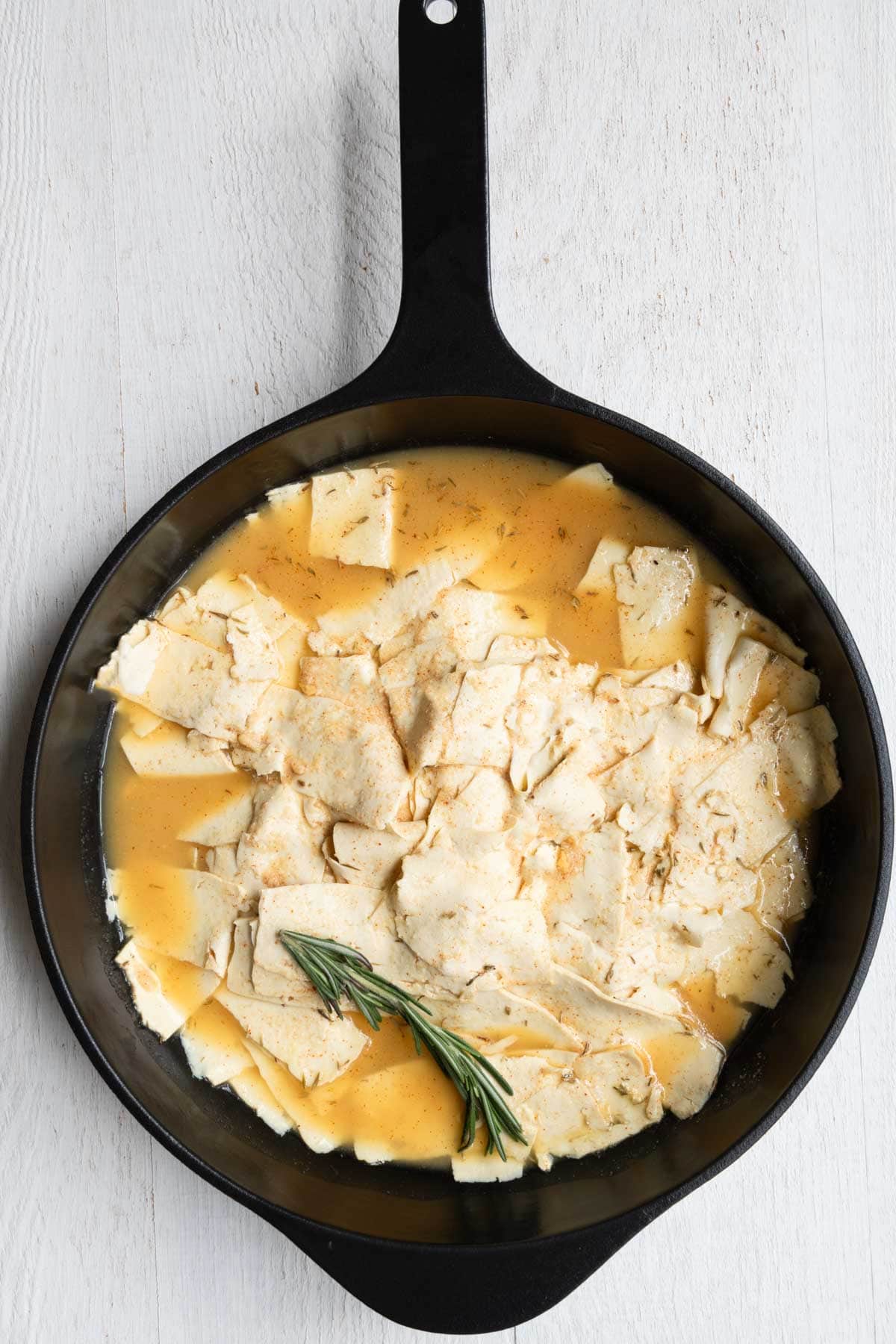 Thinly sliced tofu cooking in lemon, miso, smoked paprika, dried thyme, garlic powder, onion powder, vegetable bouillon, and nutritional yeast, topped with rosemary.