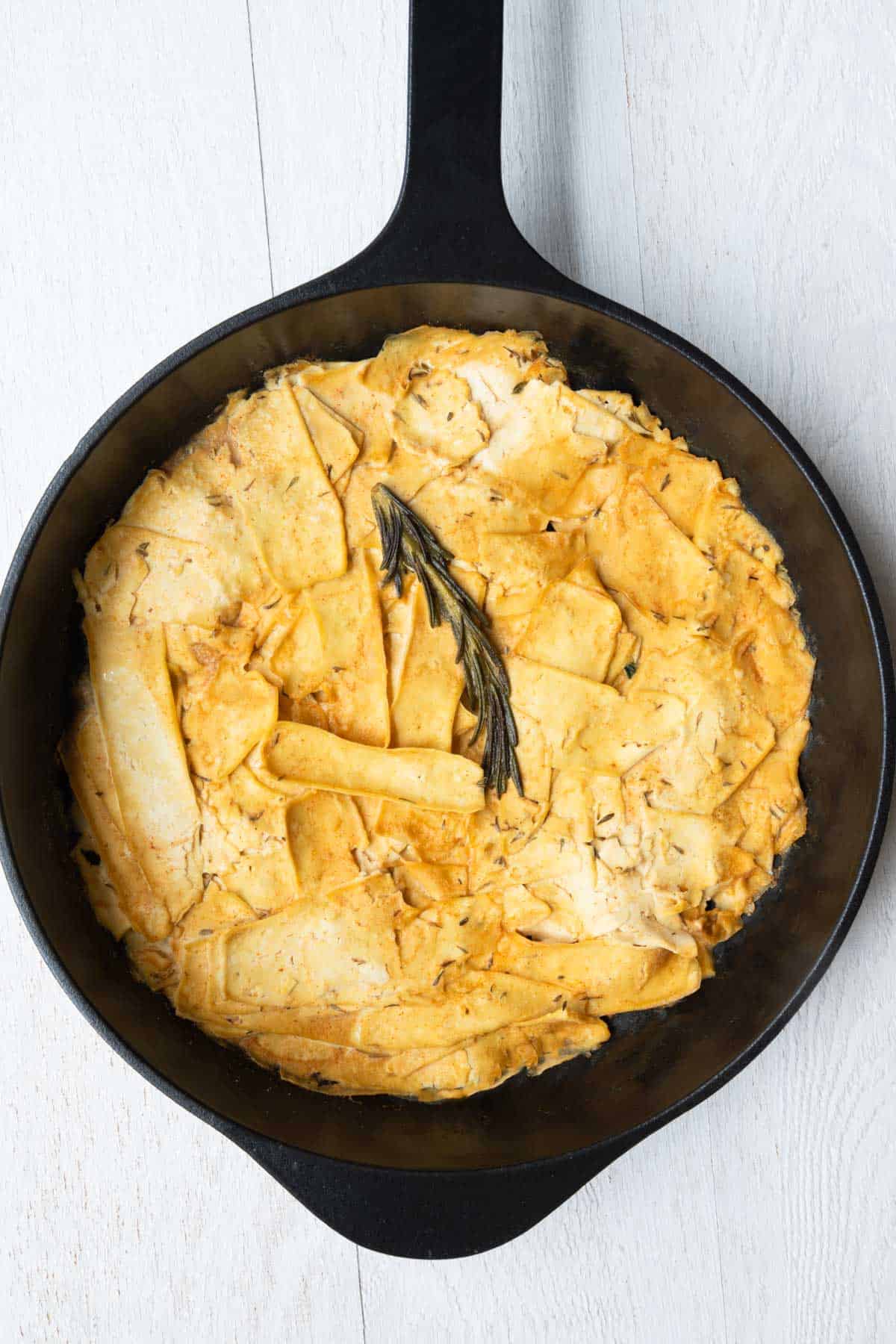 Vegan deli meat tofu slices cooking in seasoning in a black skillet.