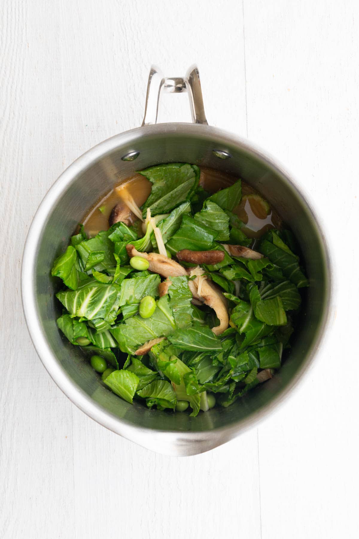 Veggie broth, seasonings, mushrooms, bok choy, and edamame in a small saucepan.