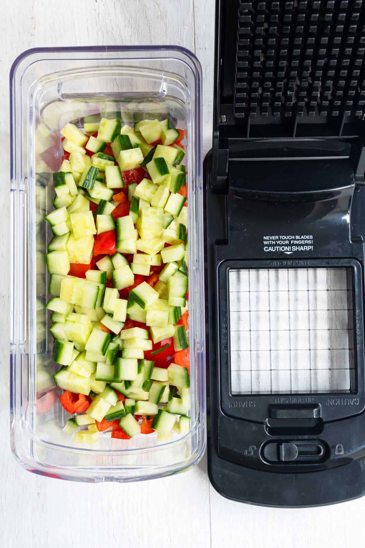 Chopped cucumber, red bell pepper, and red onion in a veggie chopper.