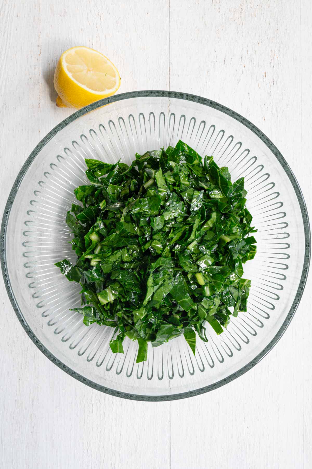 Chopped green kale in a glass bowl next to a lemon.