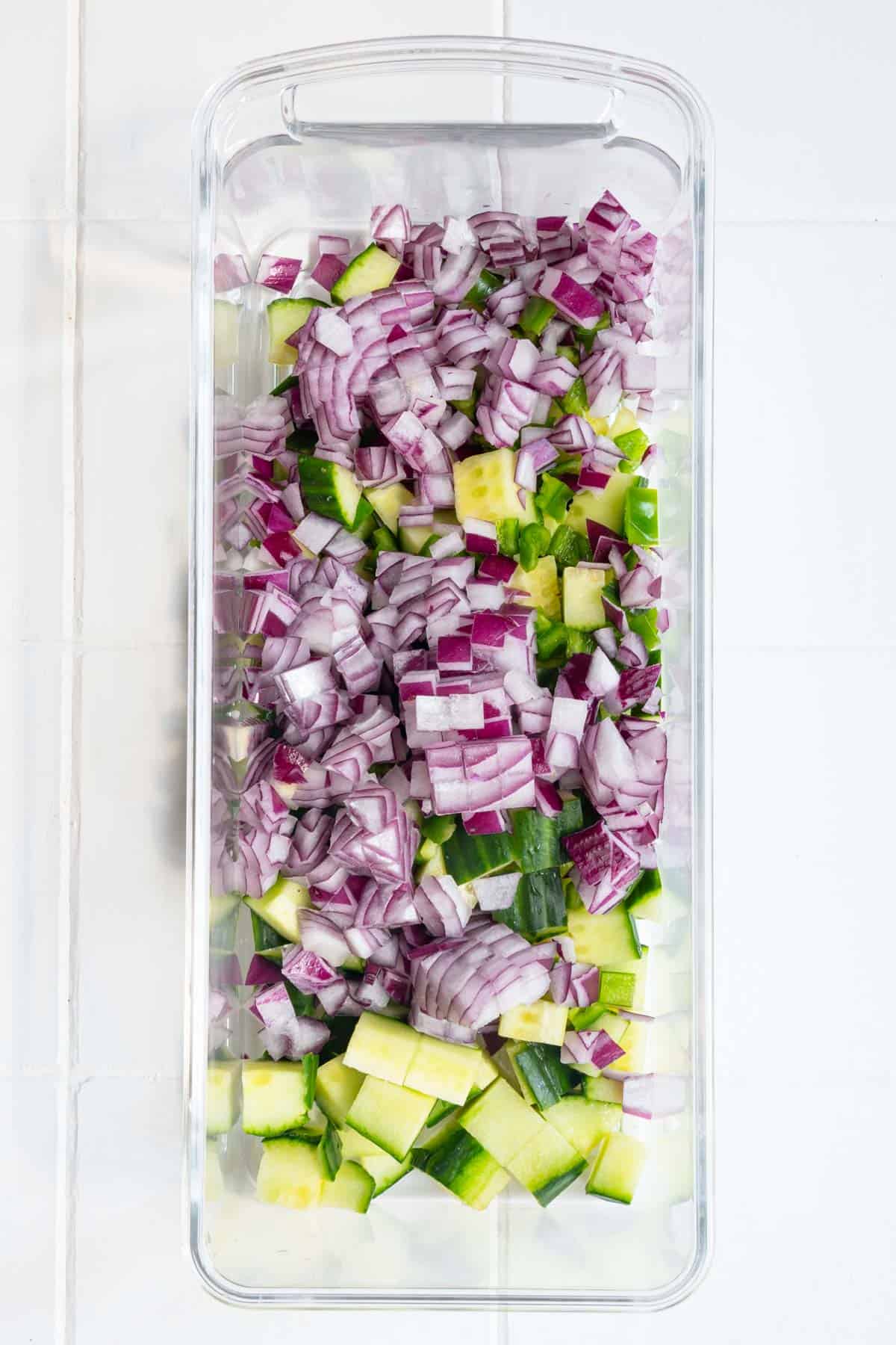 Chopped red onion and cucumber in a vegetable chopper.
