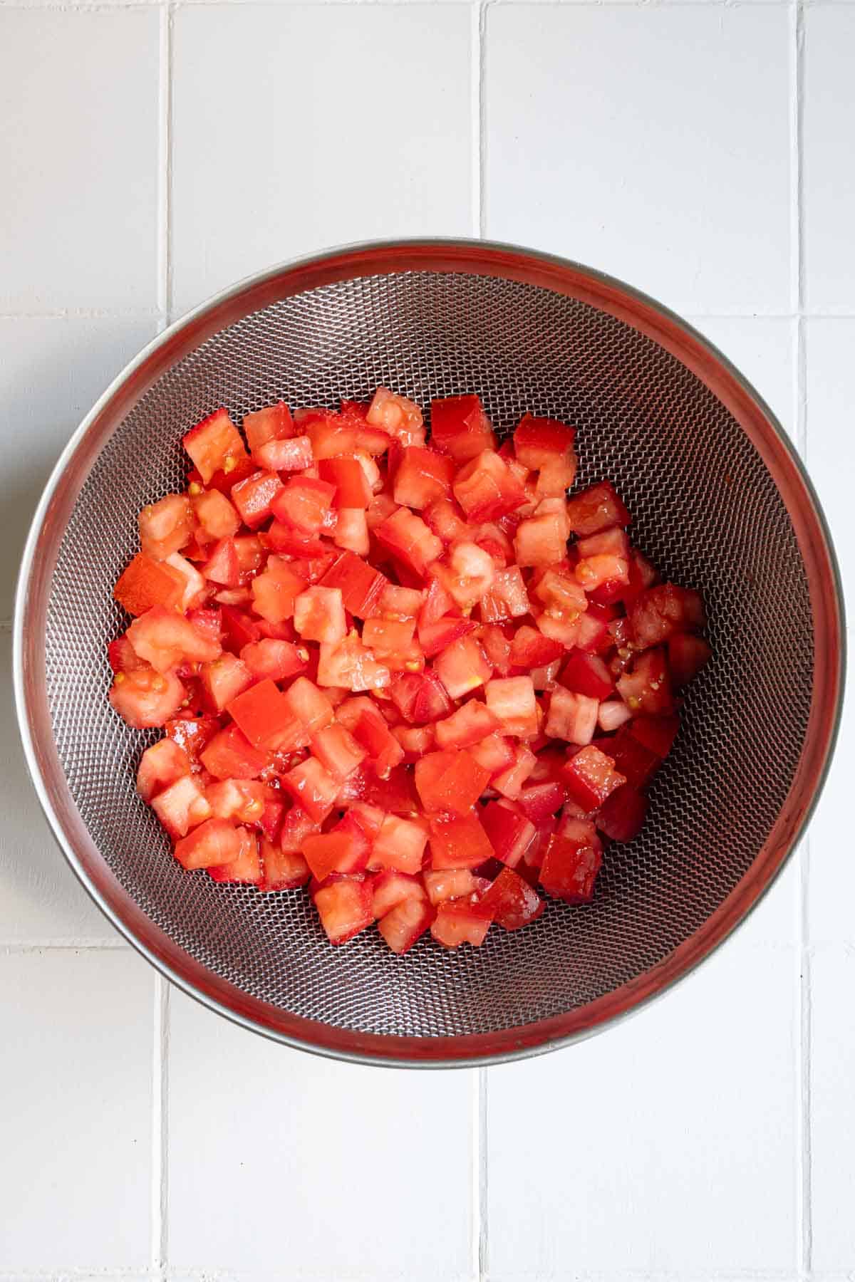 Chopped and salted tomatoes in a strainer.