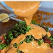 Pouring harissa dressing onto salad.