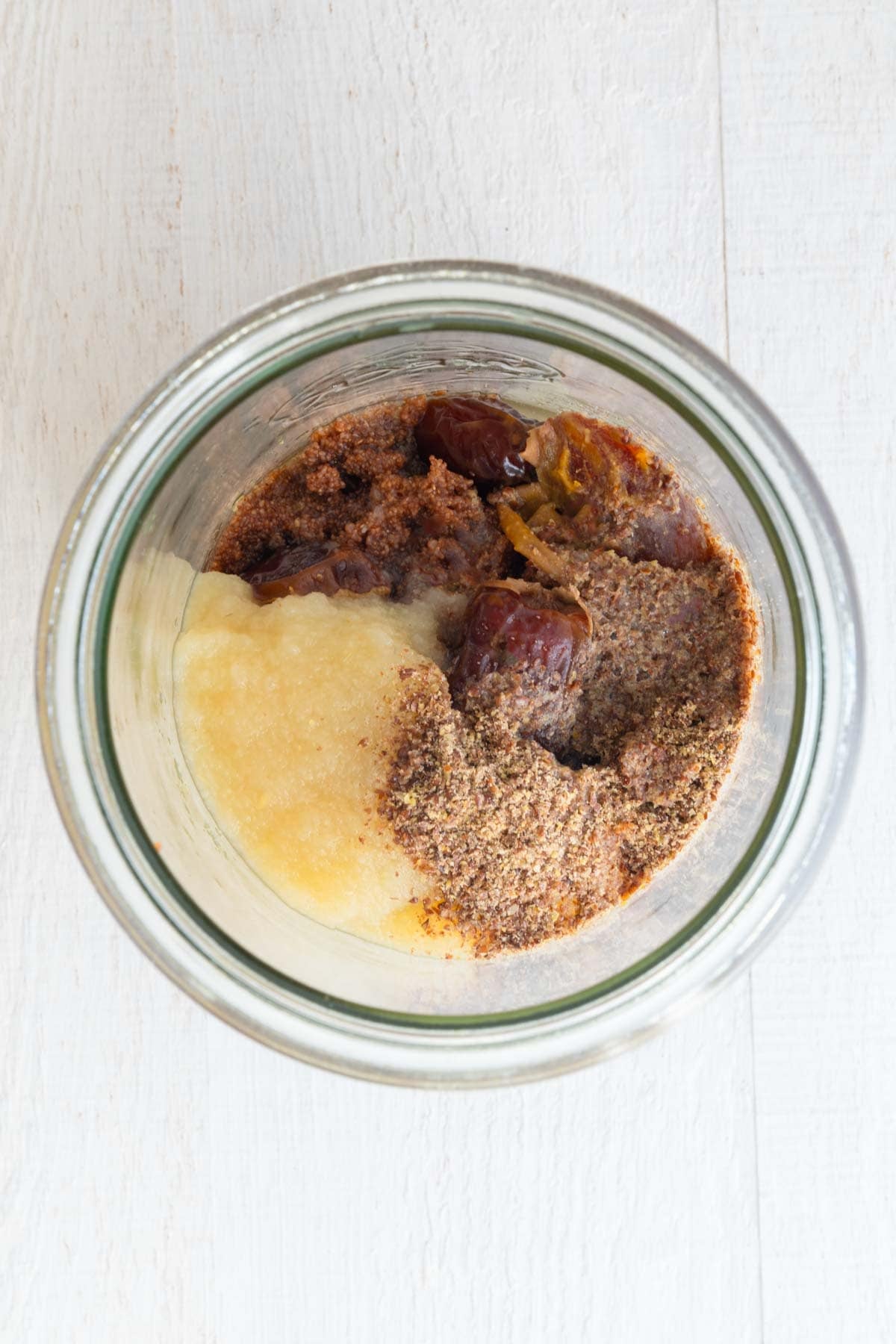 Applesauce, flaxseed meal, dates, cooked teff, and orange juice in a glass jar.