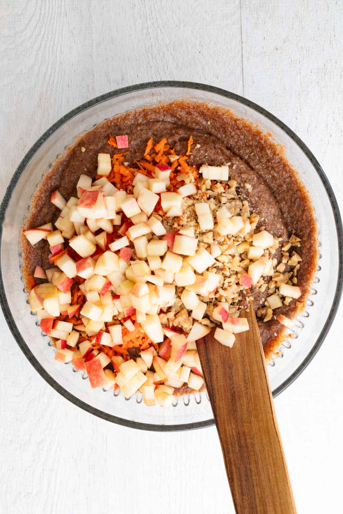 Cake batter with teff, chopped apple, and grated carrots in a glass bowl.