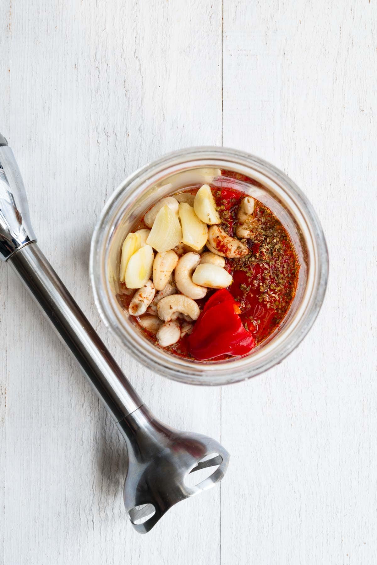 Soaked cashews, garlic, roasted bell peppers, seasoning, red chili pepper, lemon juice, and water in a glass jar.