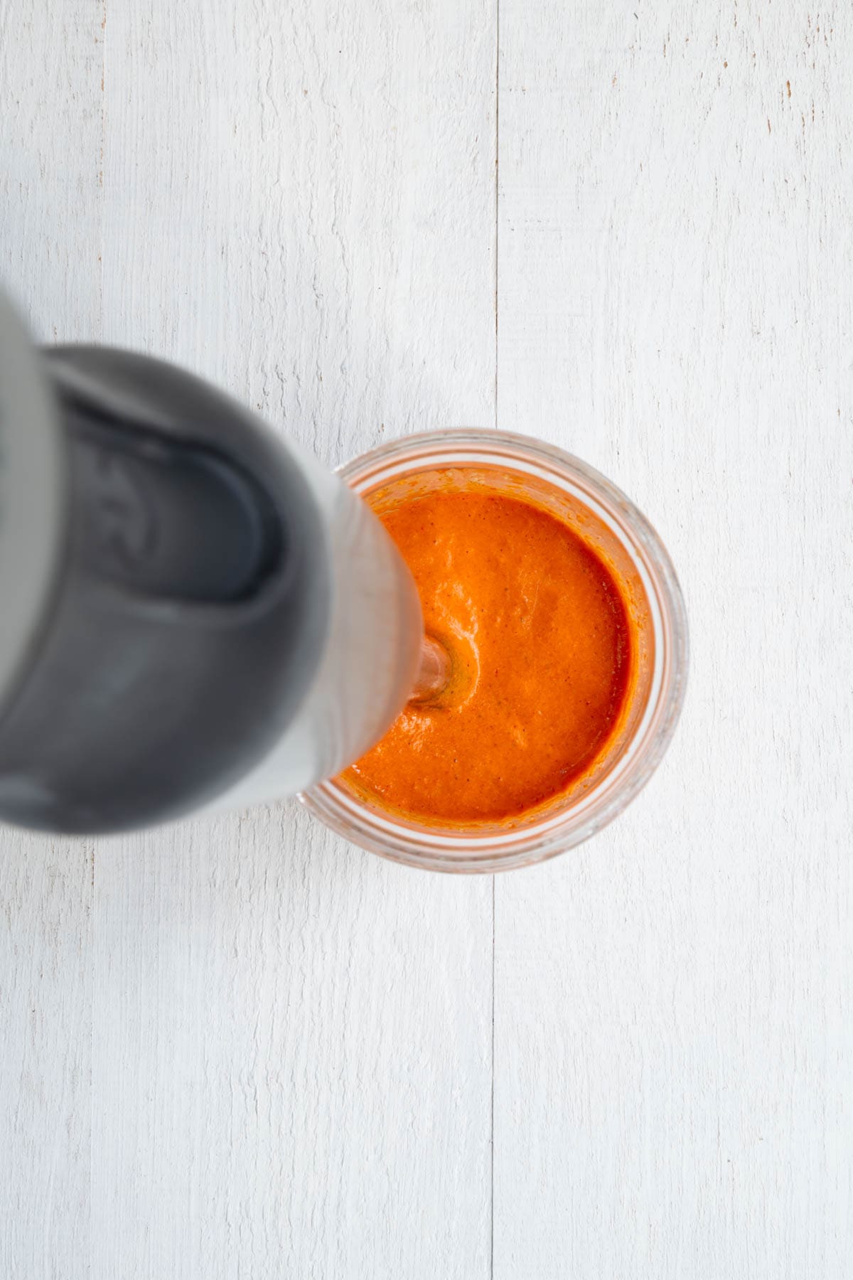 Red cream being blended with an immersion blender.