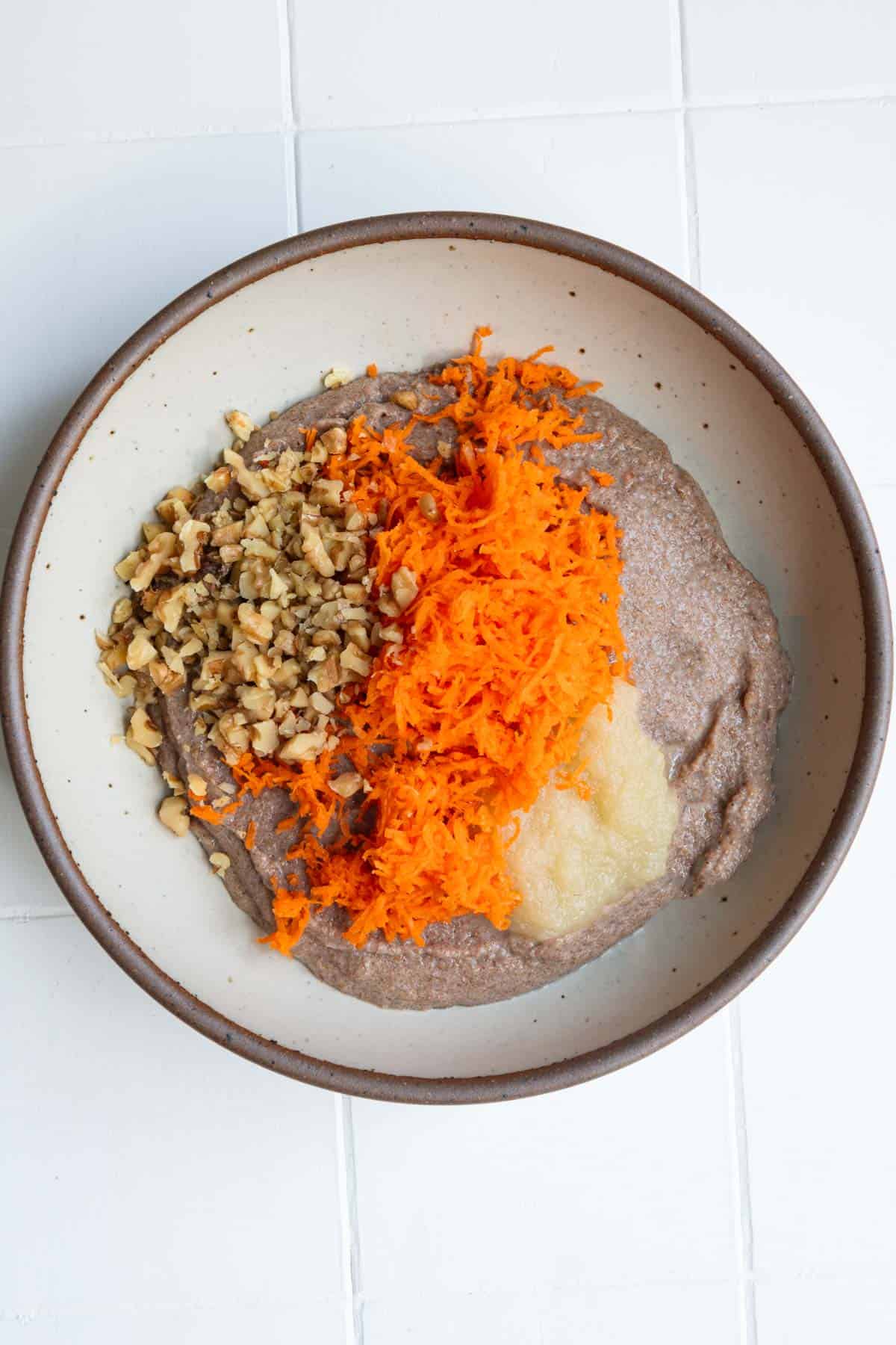 Cooked and blended teff, grated carrot, apple sauce, and chopped walnuts in a bowl.