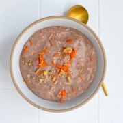 Teff porridge (carrot cake) topped with grated carrot and chopped walnuts in a bowl.