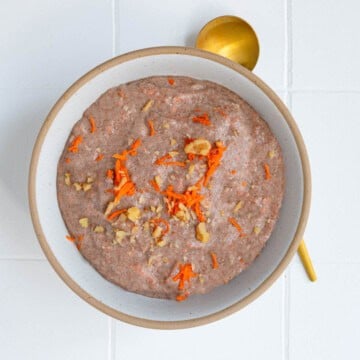 Teff porridge (carrot cake) topped with grated carrot and chopped walnuts in a bowl.