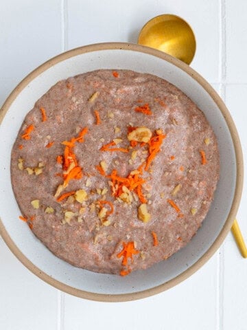 Teff porridge (carrot cake) topped with grated carrot and chopped walnuts in a bowl.