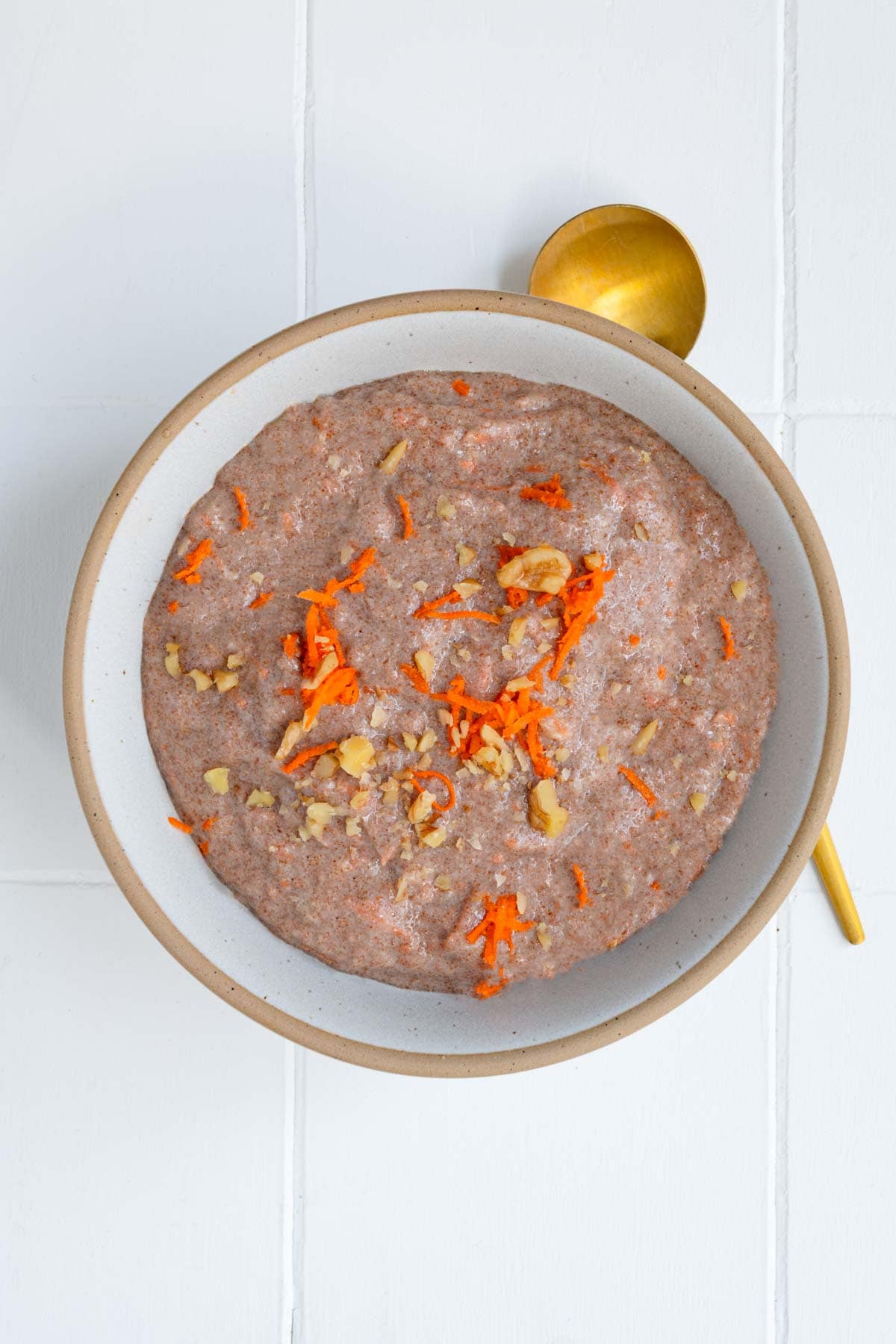 Teff porridge (carrot cake) topped with grated carrot and chopped walnuts in a bowl.