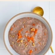 Teff porridge (carrot cake) topped with grated carrot and chopped walnuts in a bowl.