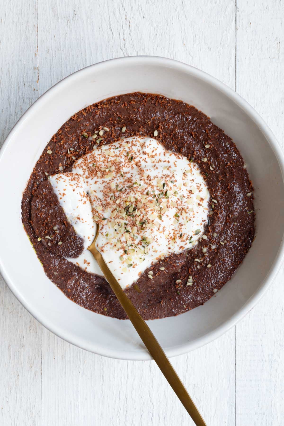 Chocolate Teff Porridge in a white bowl with yogurt, shaved chocolate, and hemp hearts.